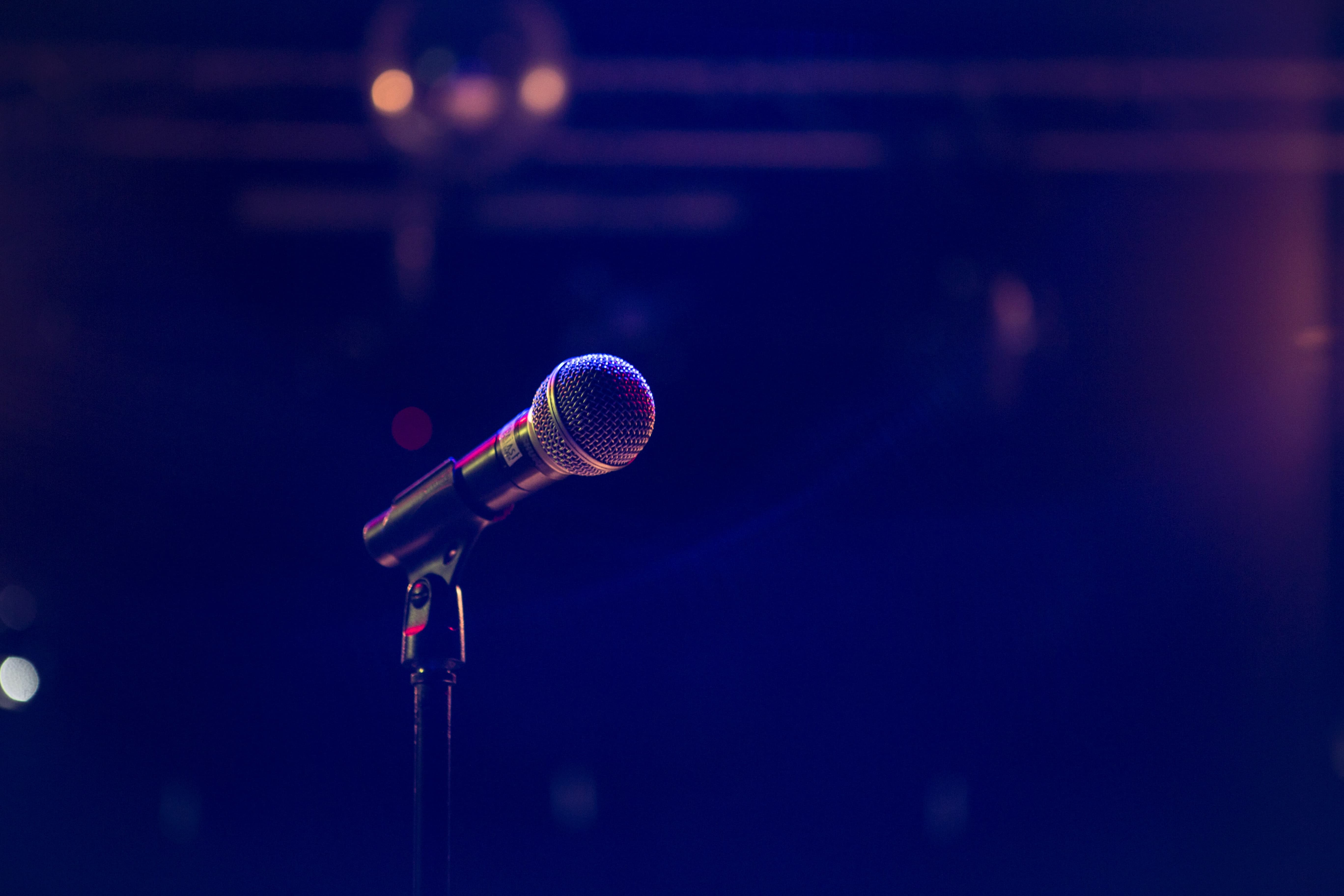 A microphone on a stand set along on a dramatically lit stage