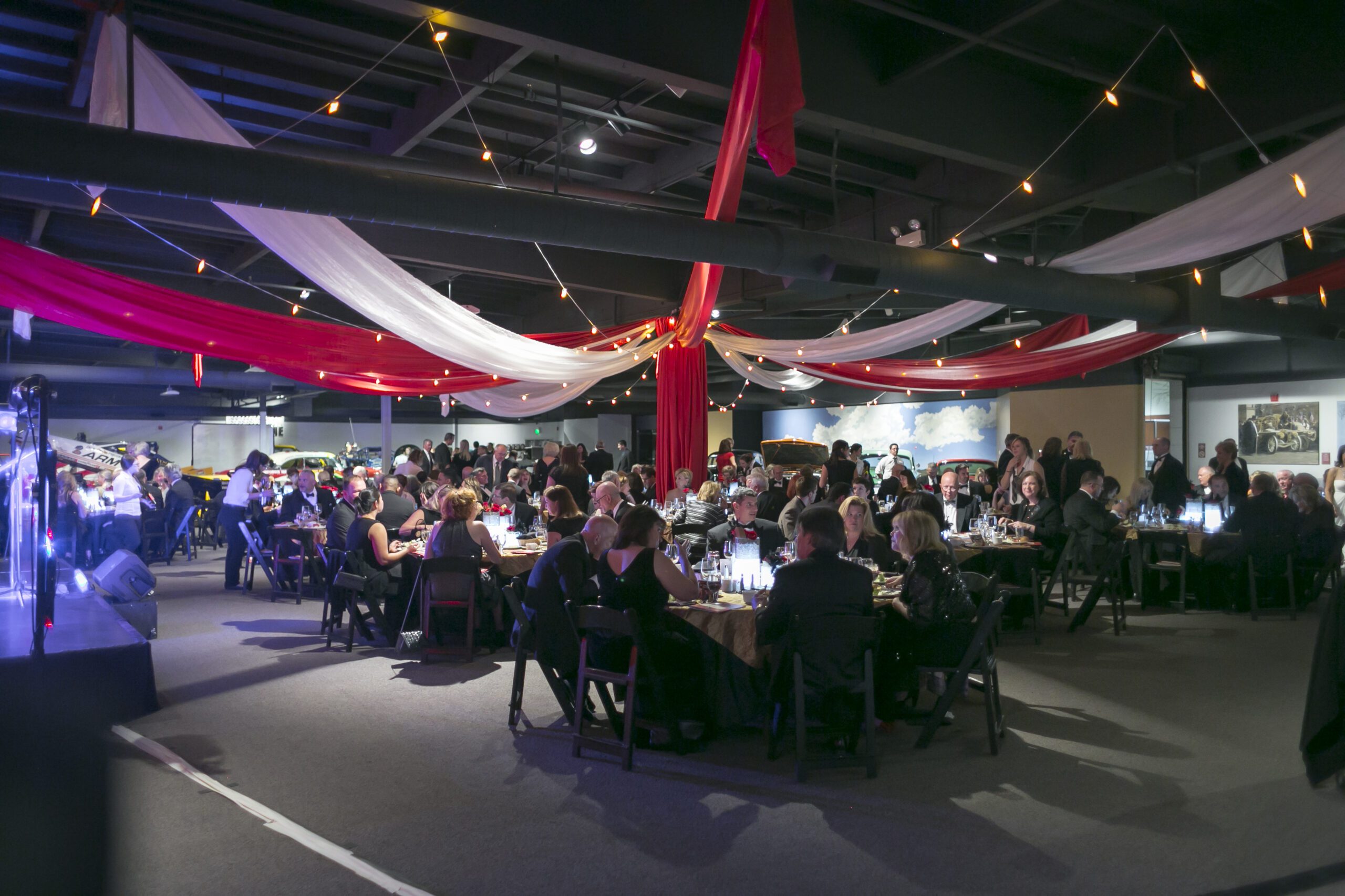 A large ballroom used as conference space. Circular tables fill the room, with people at each seat. The ceiling is adorned with red and white fabric.