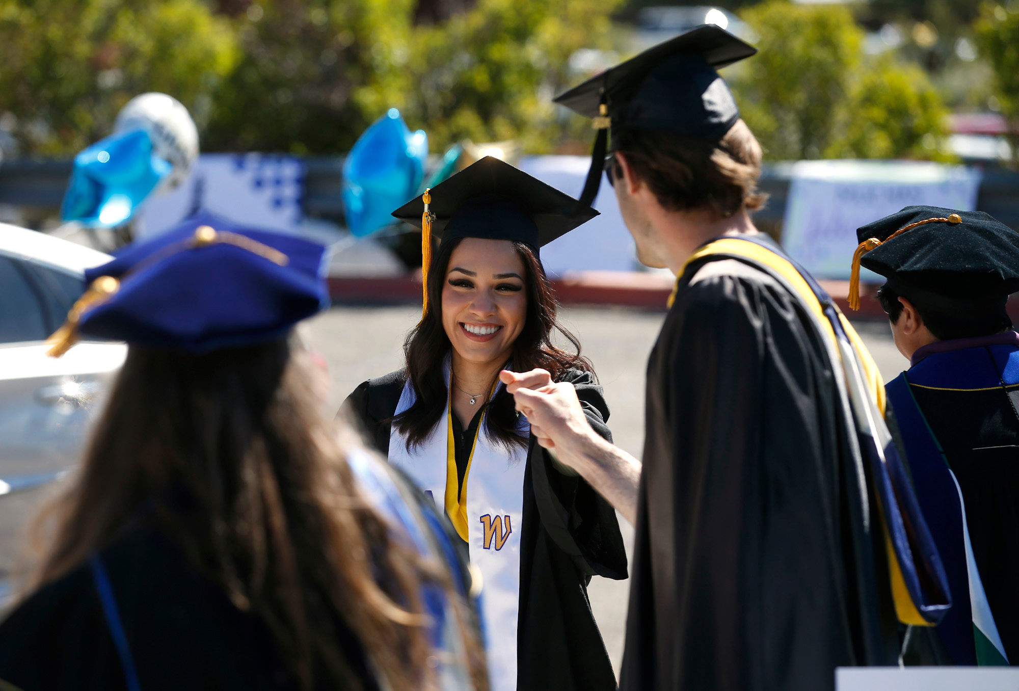 A trio of WNC graduates stand in a parking lot. Two graduates fist bump each other.